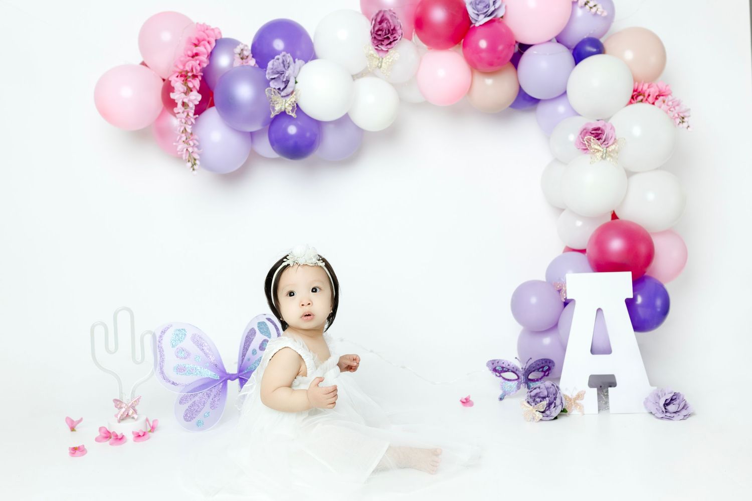 Festive balloon arrangement in pink and purple with butterfly motifs for baby photoshoot.