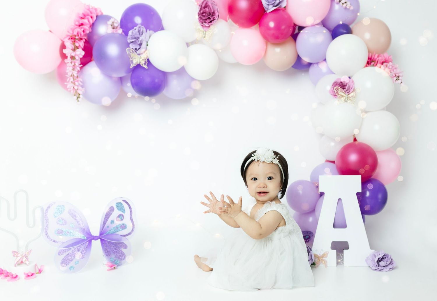 Whimsical balloon arch setup in pink, purple and white with butterfly decorations.