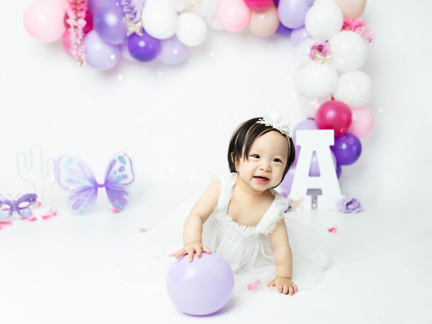 Purple and pink balloon arch with butterfly decorations for baby photography.