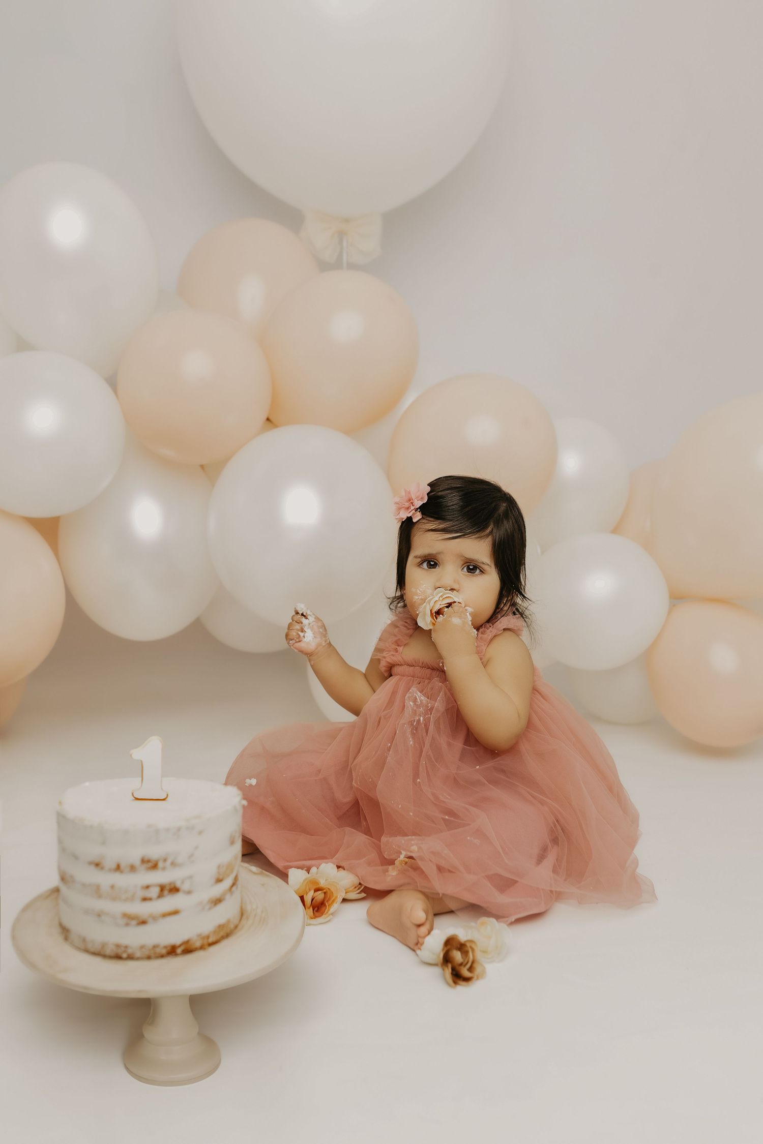 First birthday cake smash setup with naked cake, peach dress, and balloon decorations.