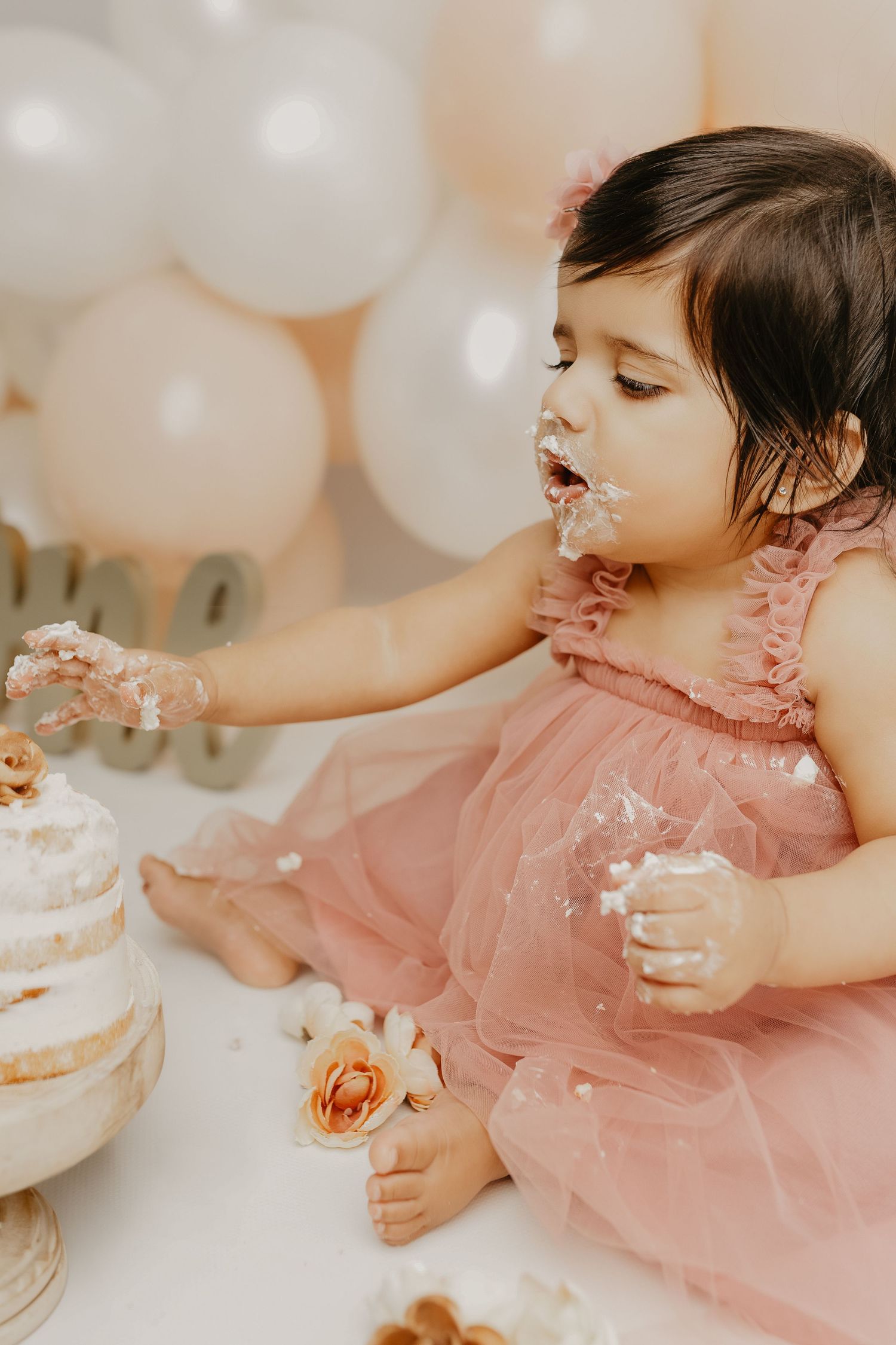 Joyful cake smash moment with frosting and semi-naked birthday cake on white pedestal.