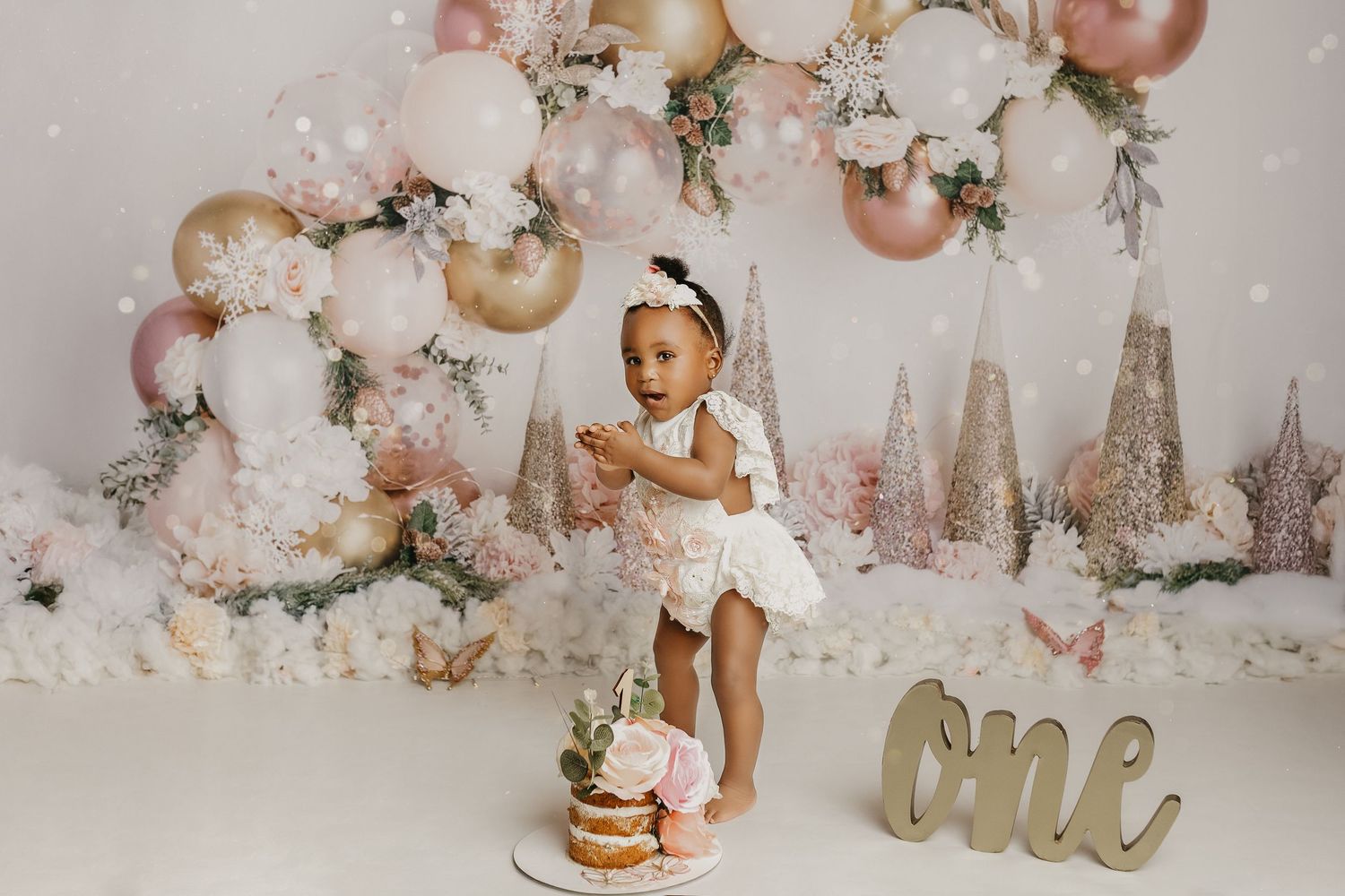 First birthday celebration with cake, balloons, and winter wonderland theme in pink and gold.