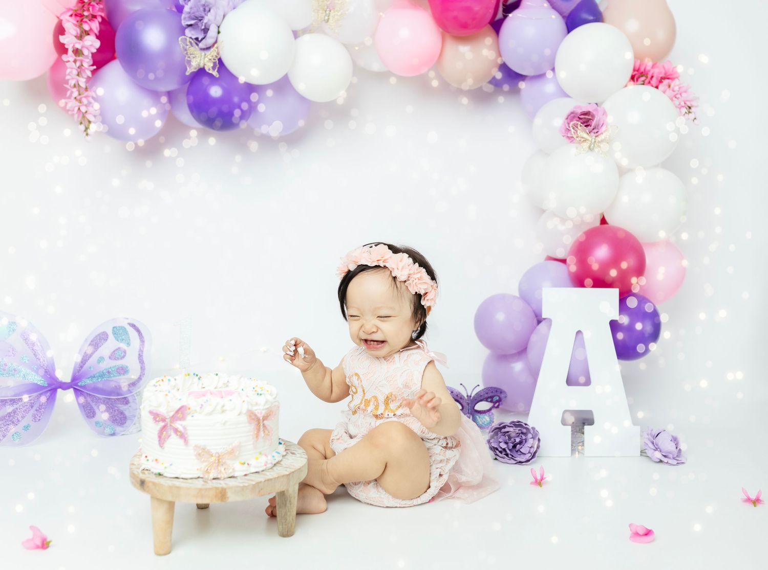 Pink and purple balloon garland with butterfly accents for baby photo session.