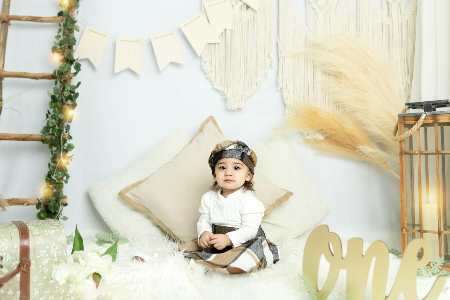 Elegant first birthday setup with white drapes, gold accents and wooden decorations.