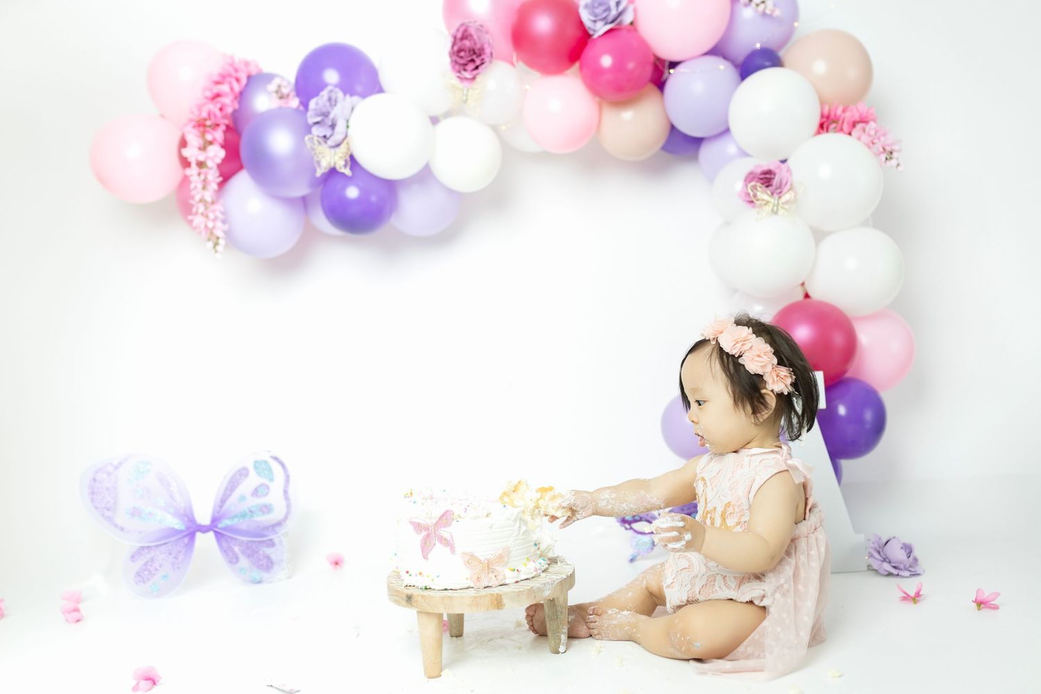Baby cake smash photo setup with pink and purple balloons against white backdrop.