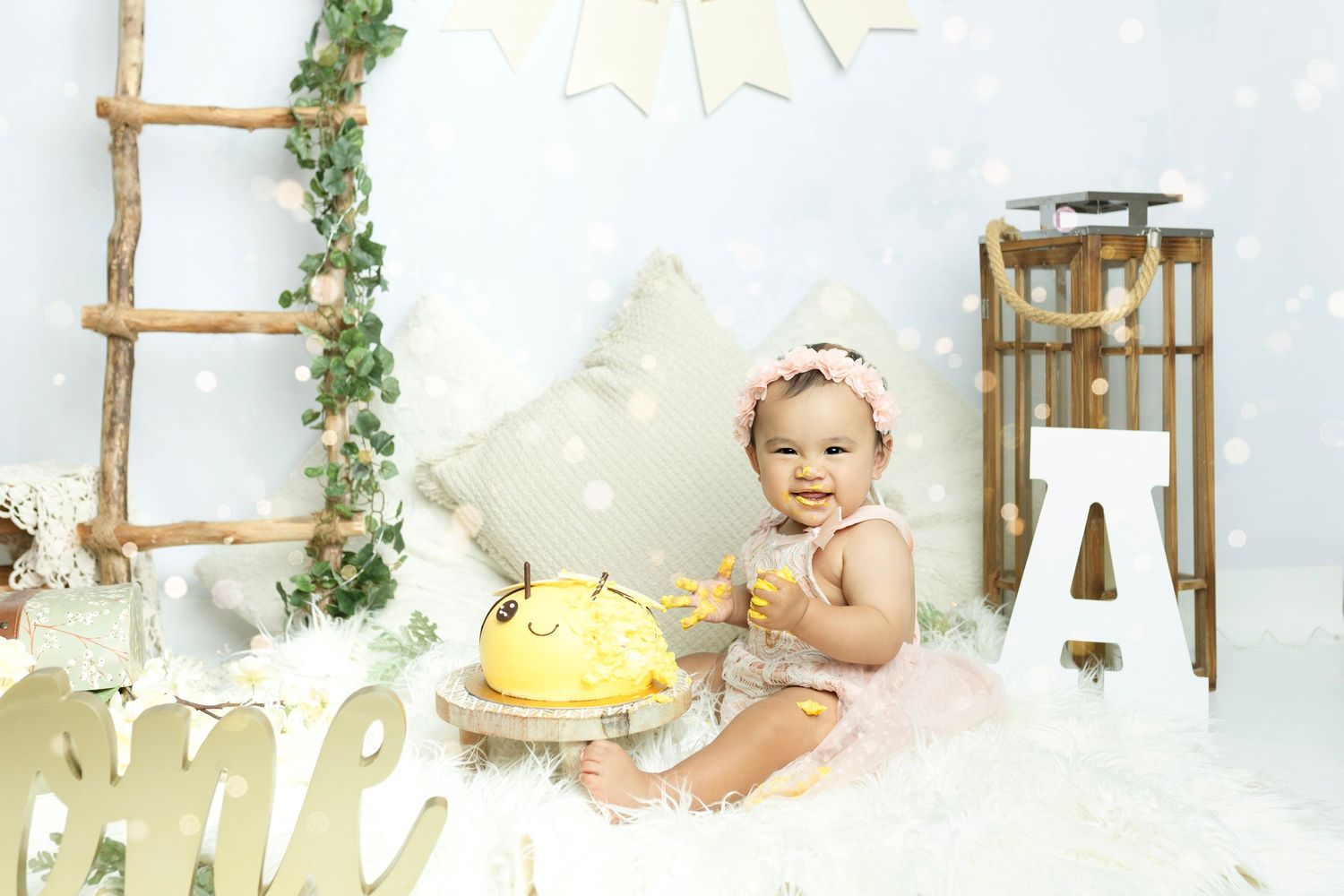 First birthday photo setup with rustic ladder, greenery, and golden decorative elements.