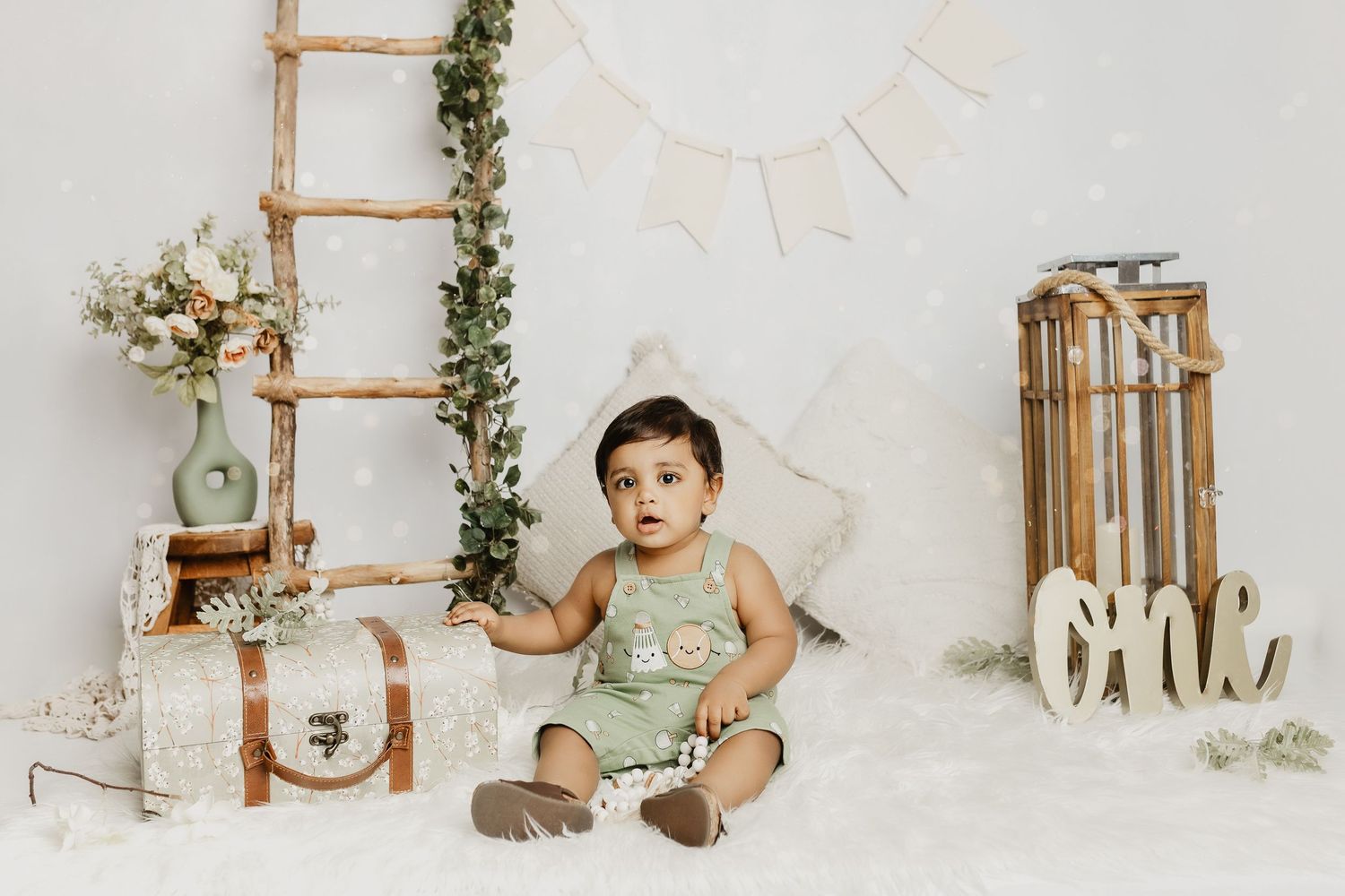 Safari themed first birthday photo setup with wooden ladder, greenery, and natural decorations.