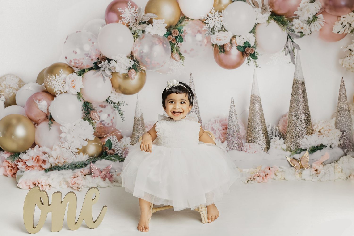Pink and gold winter wonderland themed cake smash setup with glittery trees and balloons.
