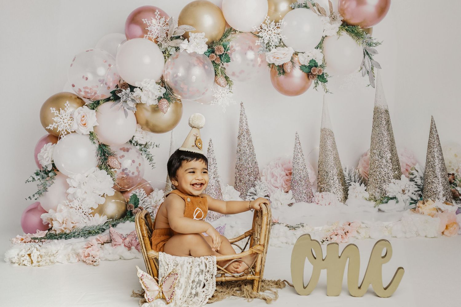 Festive first birthday setup with pink and gold decorations, sparkly trees, and floral accents.