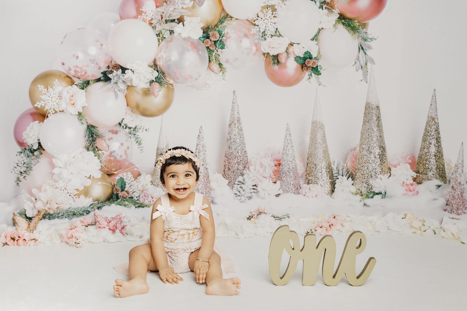 Winter wonderland first birthday scene with pink and gold decor and sparkly Christmas trees.