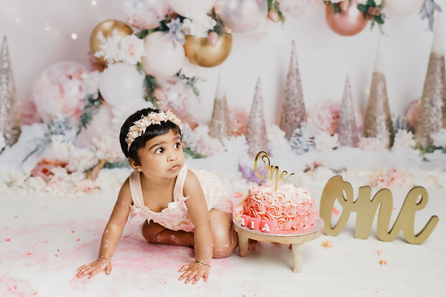 Cake smash photo session with pink frosted cake and sparkly winter wonderland backdrop.