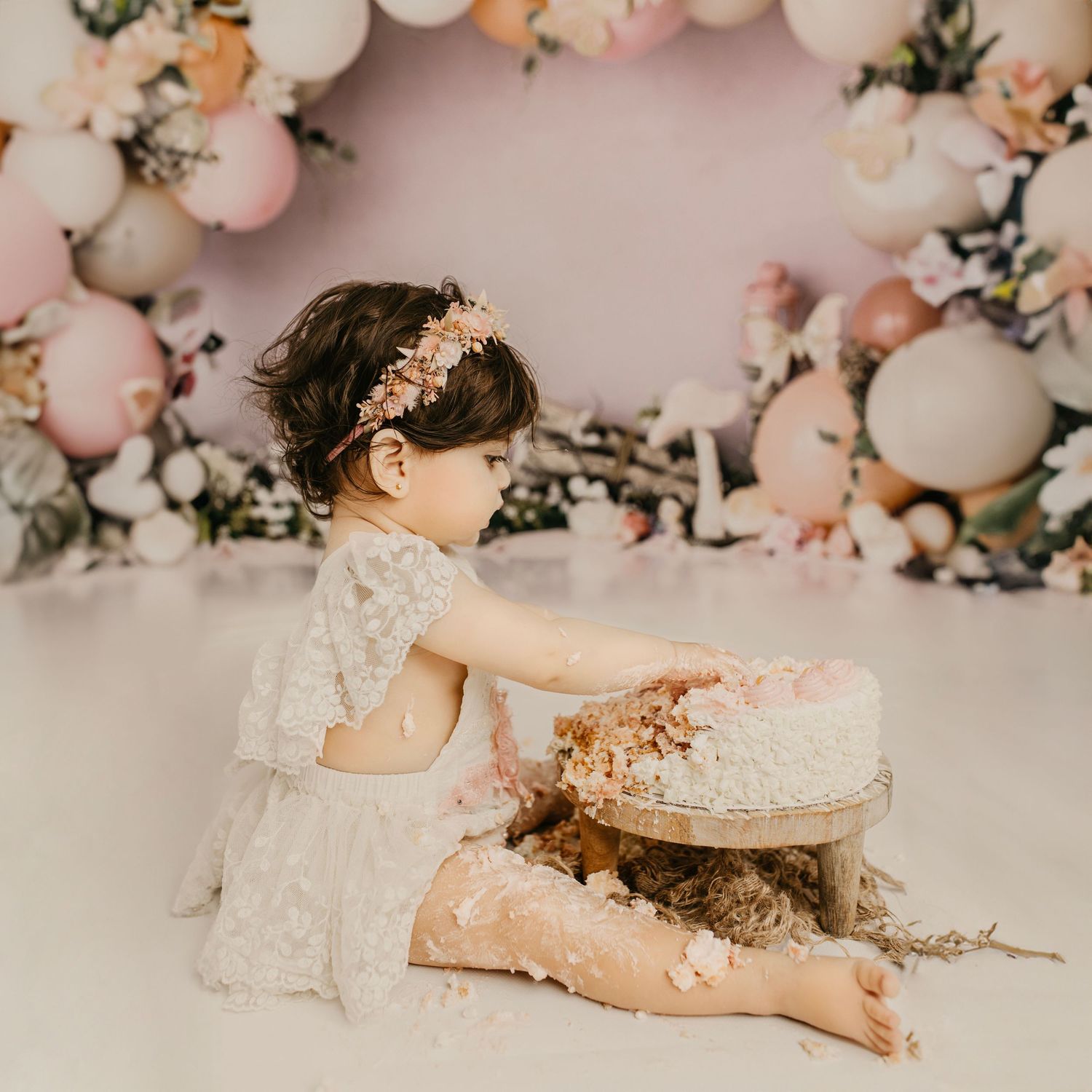 Baby cake smash photography scene with pink balloons and white frosted cake.