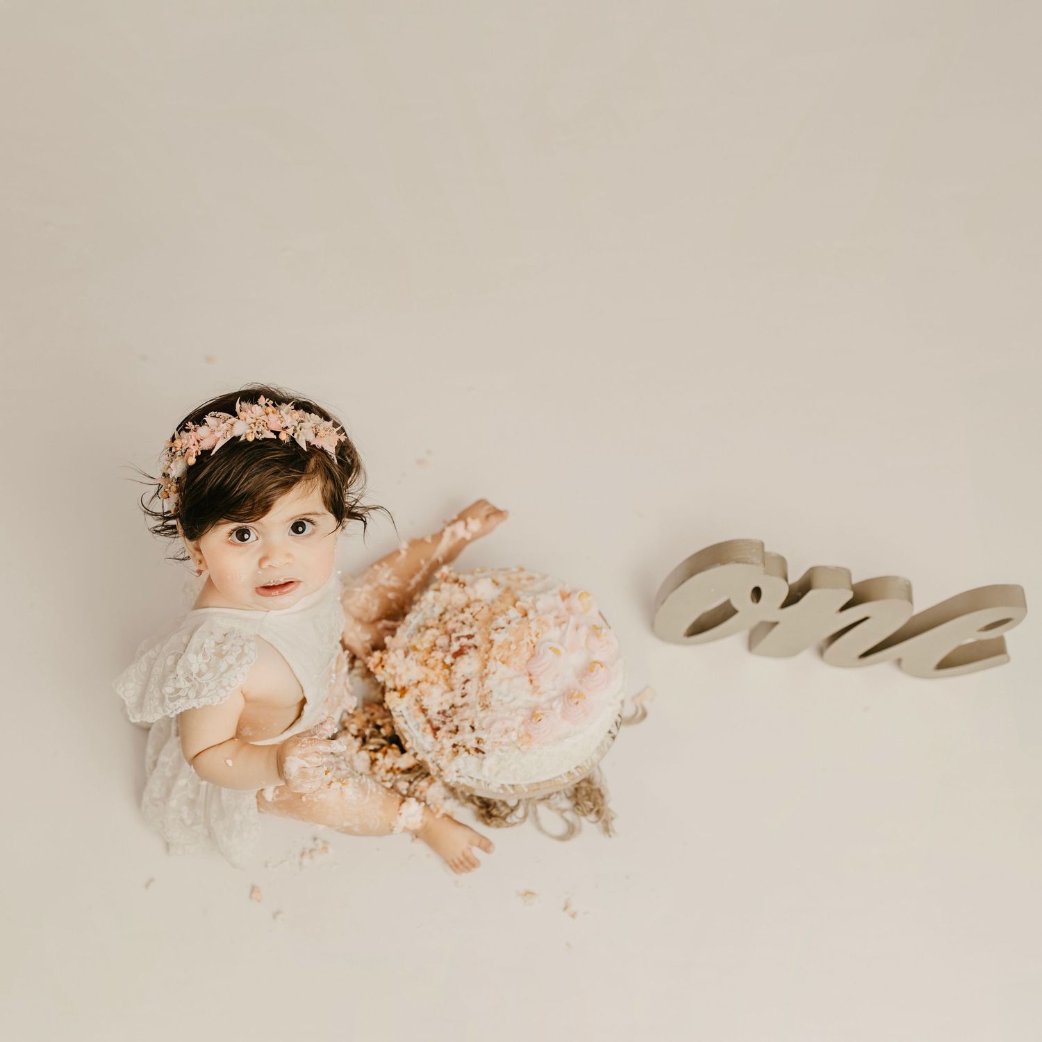 Artistic cake smash photo session with vintage-inspired decor and 'one' text sign.