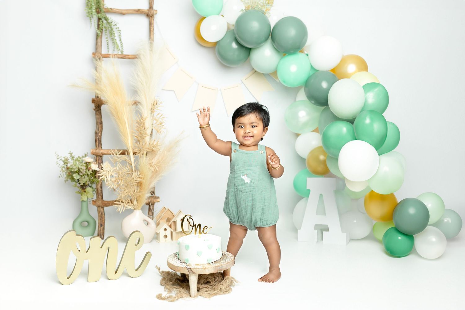 First birthday party setup with mint green and gold balloons, ladder, and decorative elements.