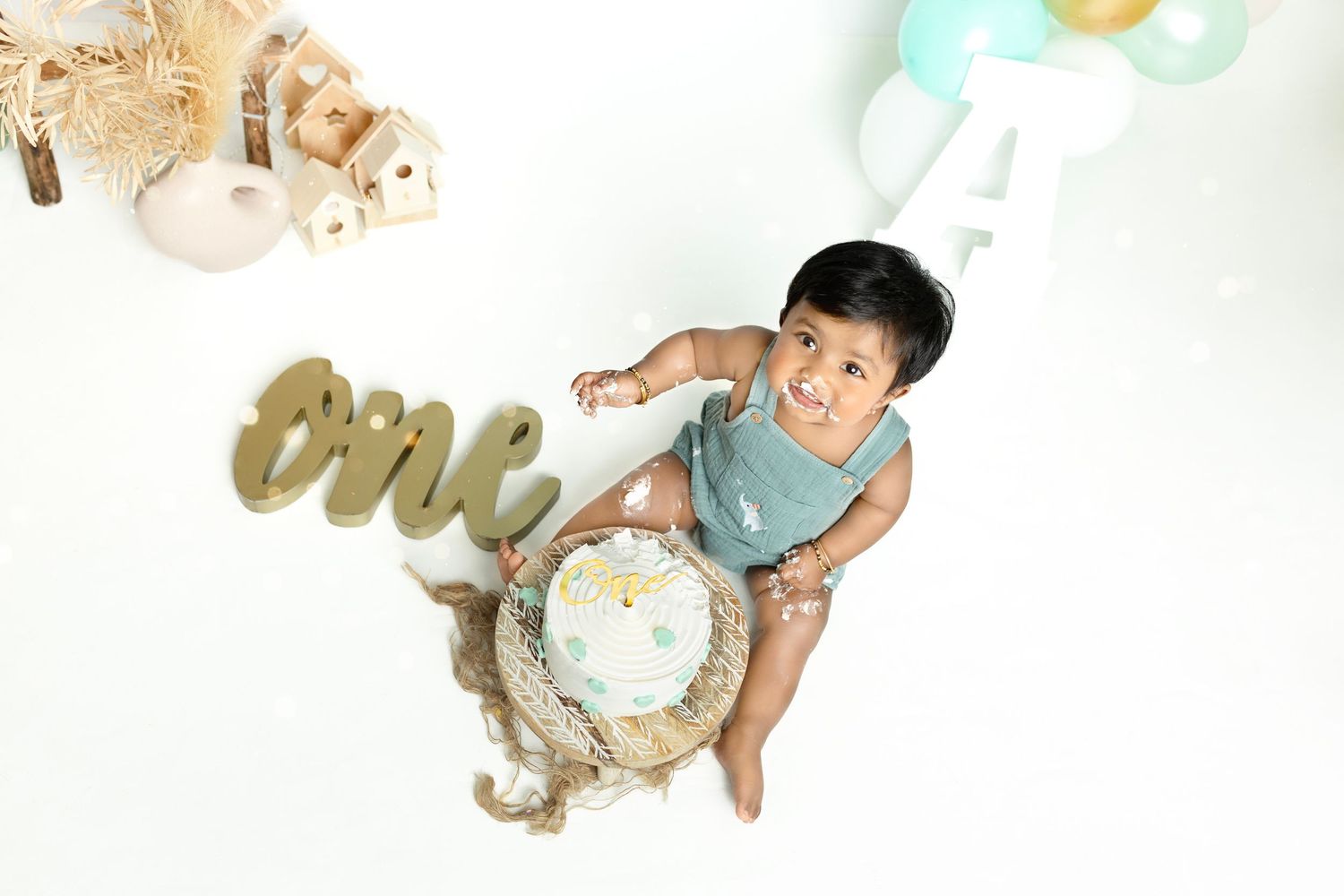 Cake smash photo session with mint green balloons and rustic wooden decorations.