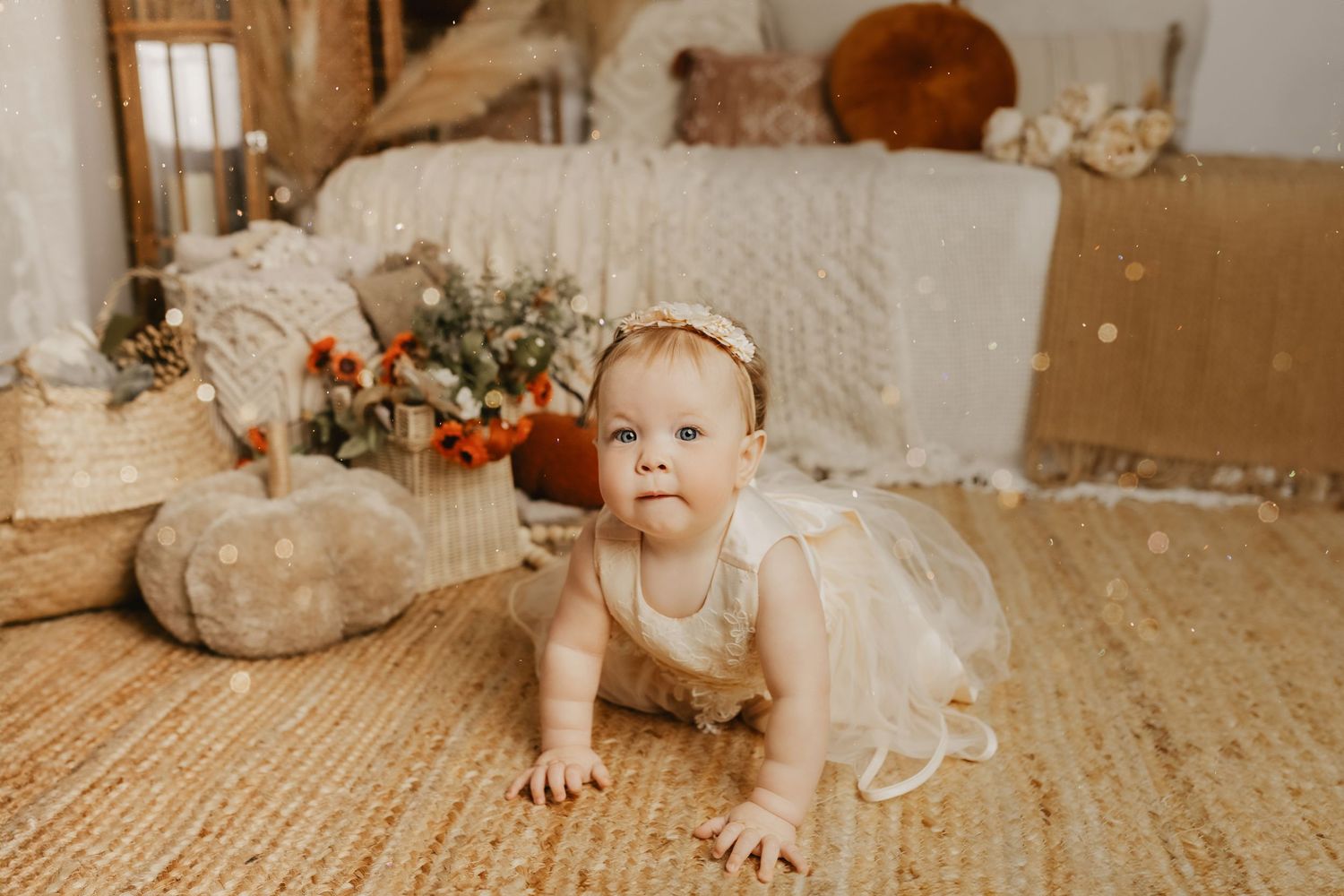 A baby girl in a white tutu dress crawls on a woven rug in a boho-styled room with soft decor.