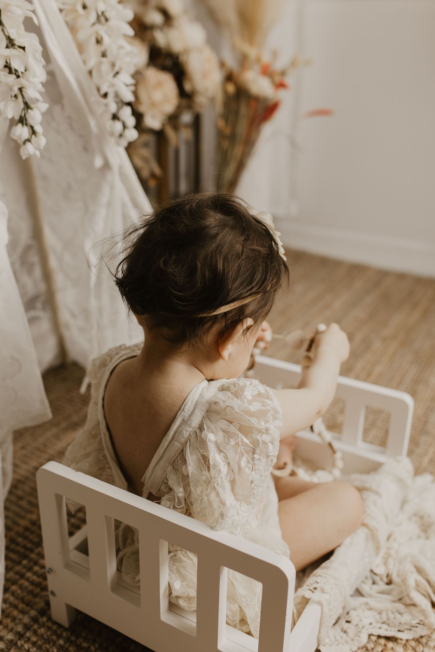 A person in a white lace dress sits at a white vanity table surrounded by delicate floral decorations.