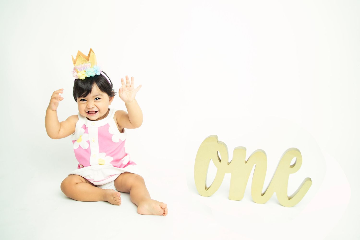 First birthday celebration setup with gold 'one' sign and festive decorations against white backdrop.