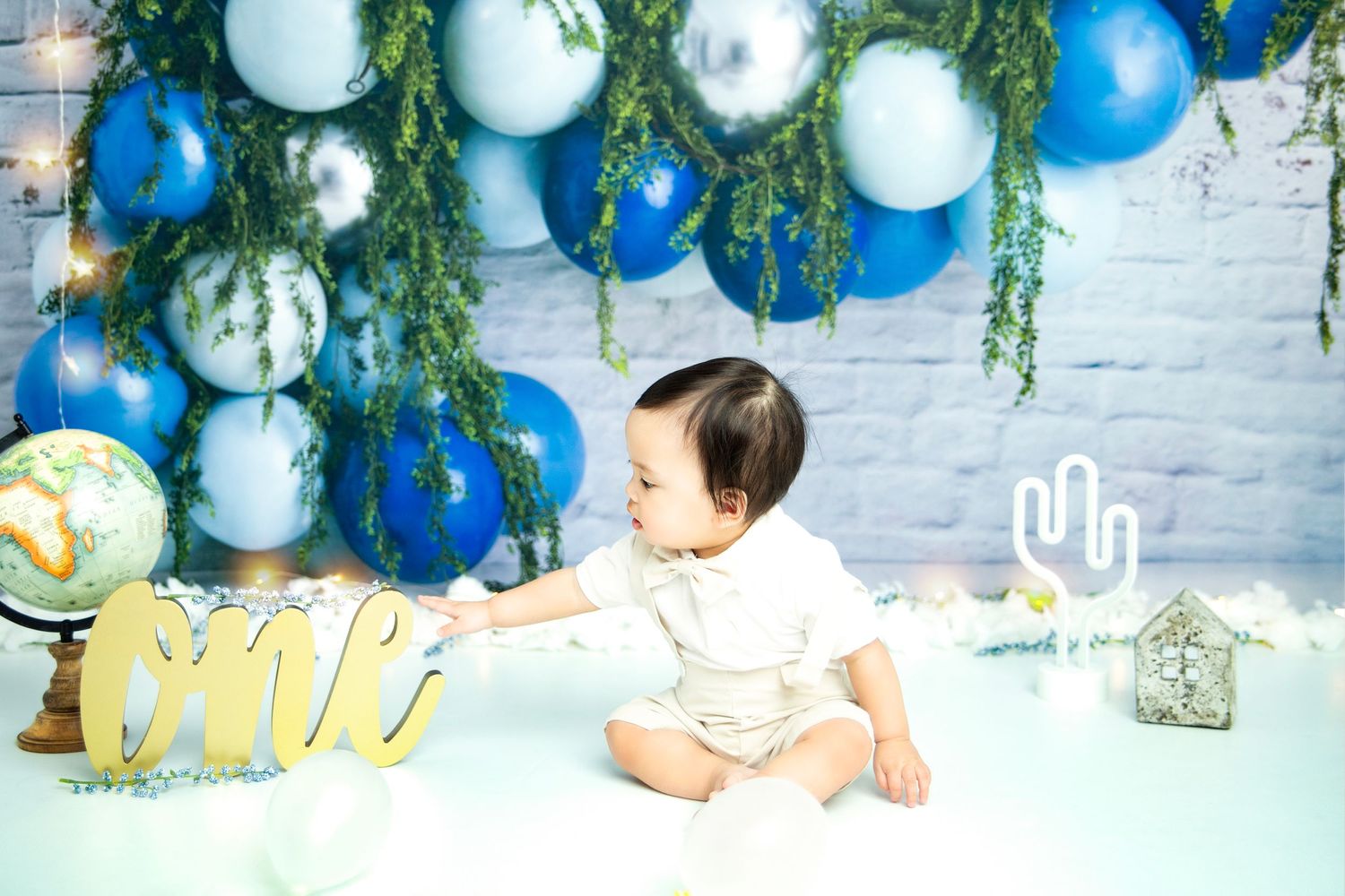 Blue and white balloon arch with greenery against white brick wall.