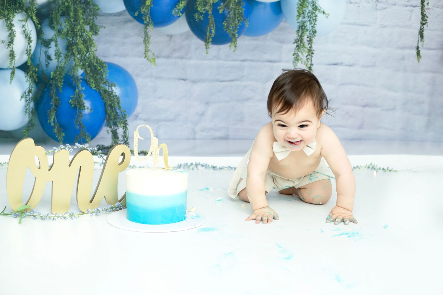 Cake smash photo session with blue balloon garland and white brick background.