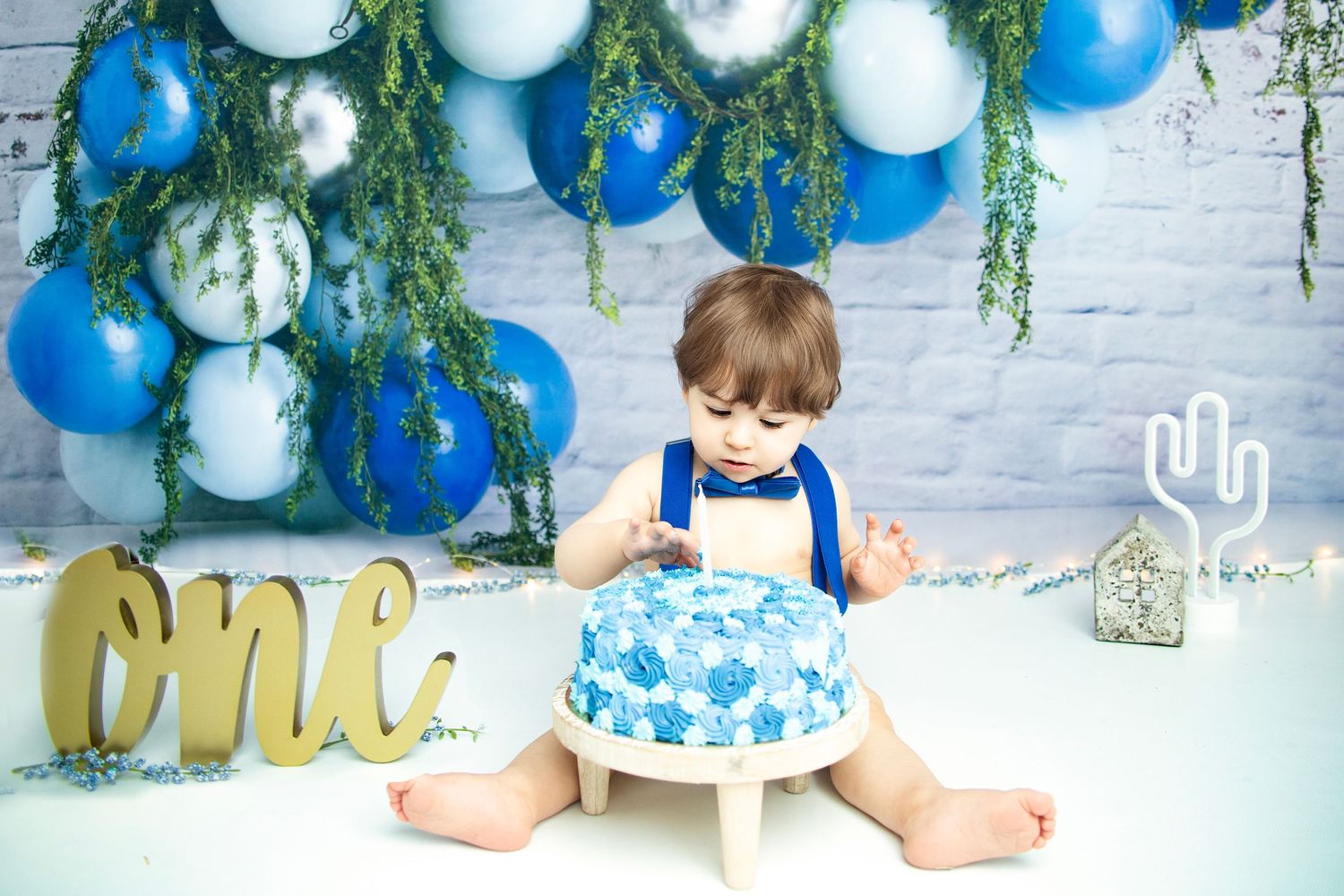 Cake smash photo setup with blue and white decorations and gold 'one' lettering.