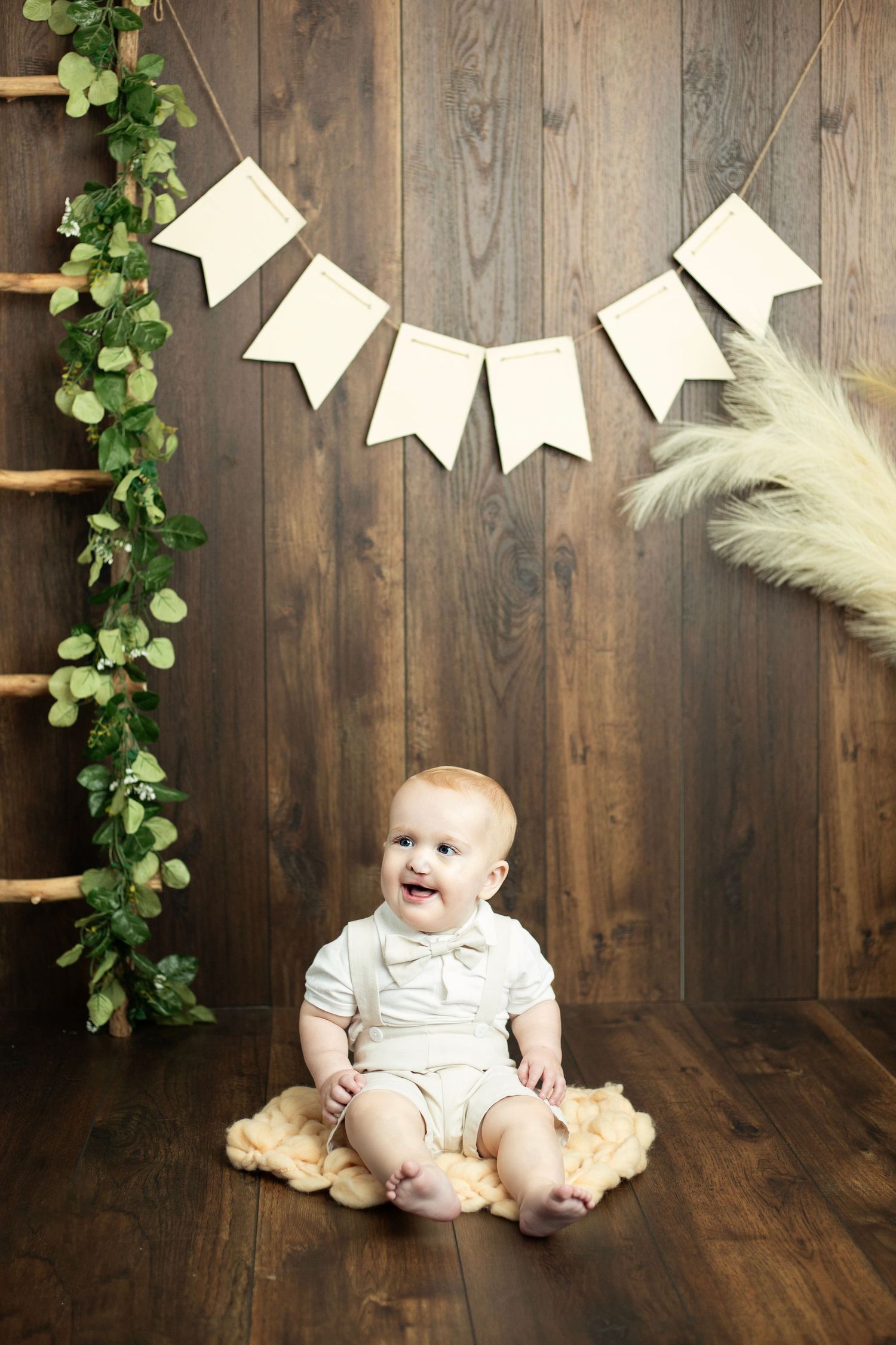 Rustic wooden backdrop with white banners and green vine decorations for baby photos.