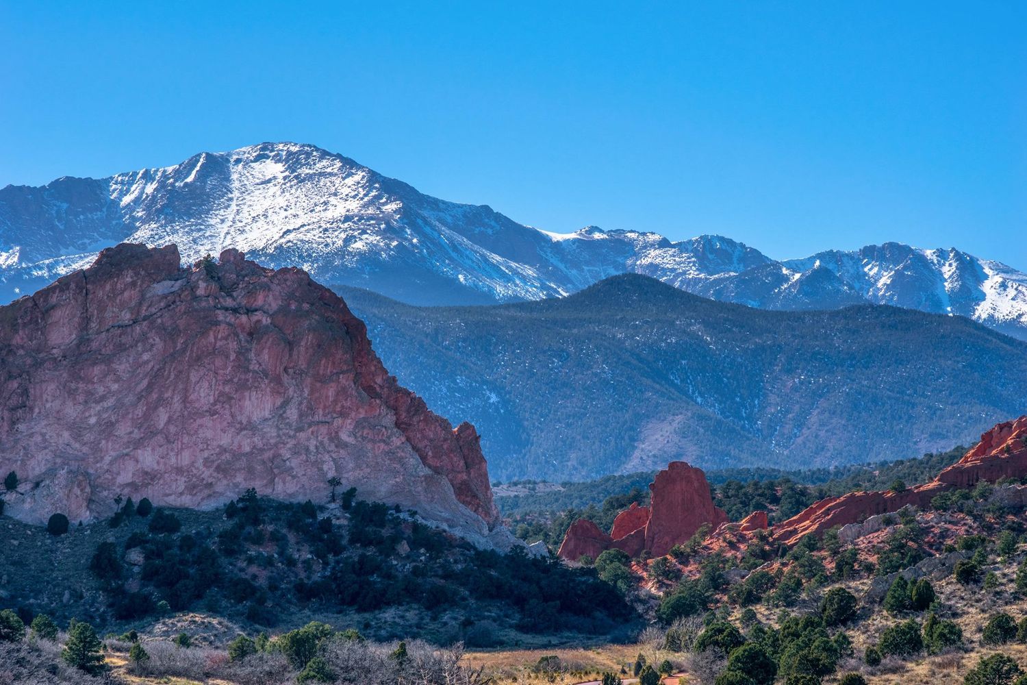 Majestic snow-covered mountain peaks tower over red rock formations in Colorado Springs.