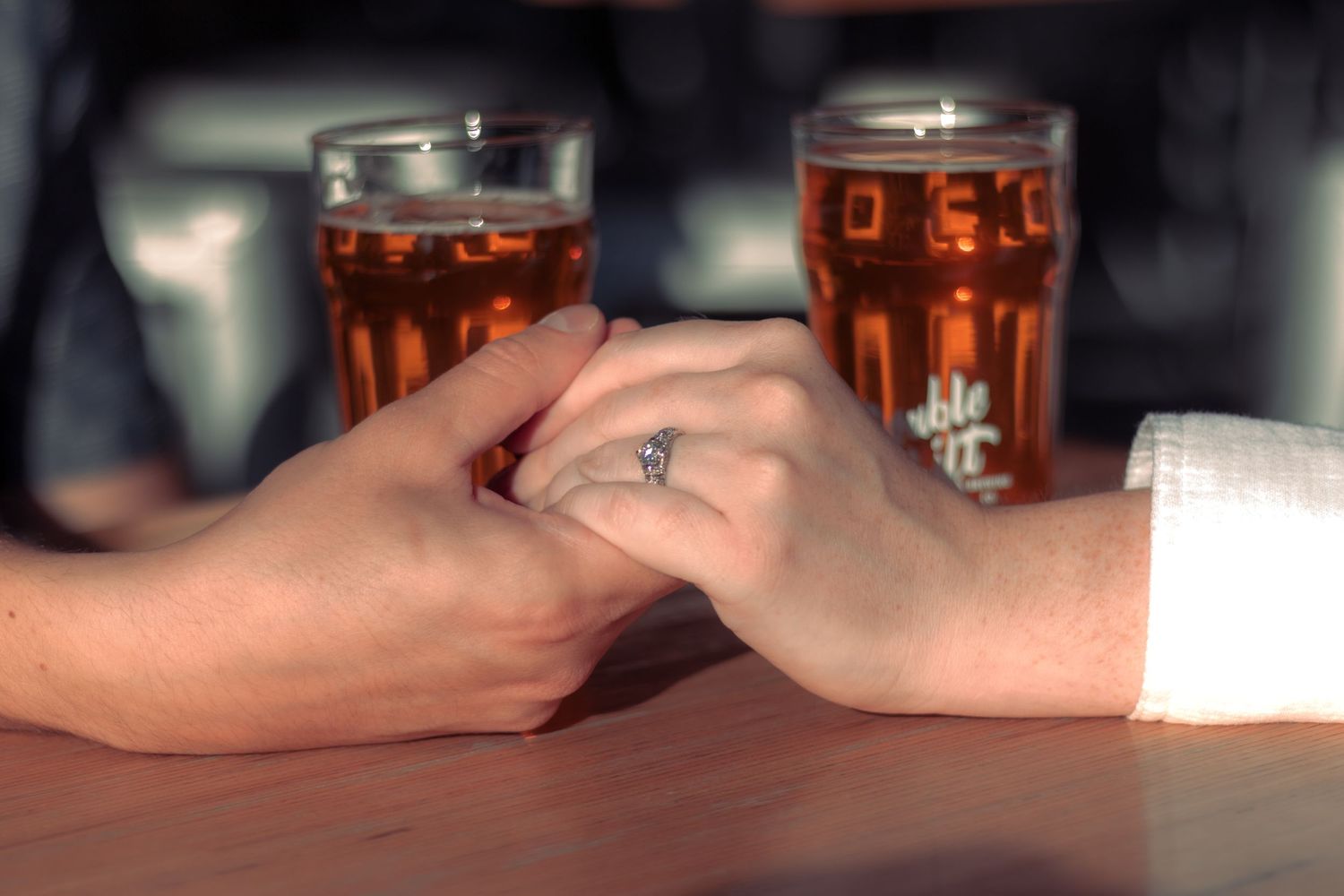 Blurred close-up shot of glasses with amber-colored drinks on a dark surface.