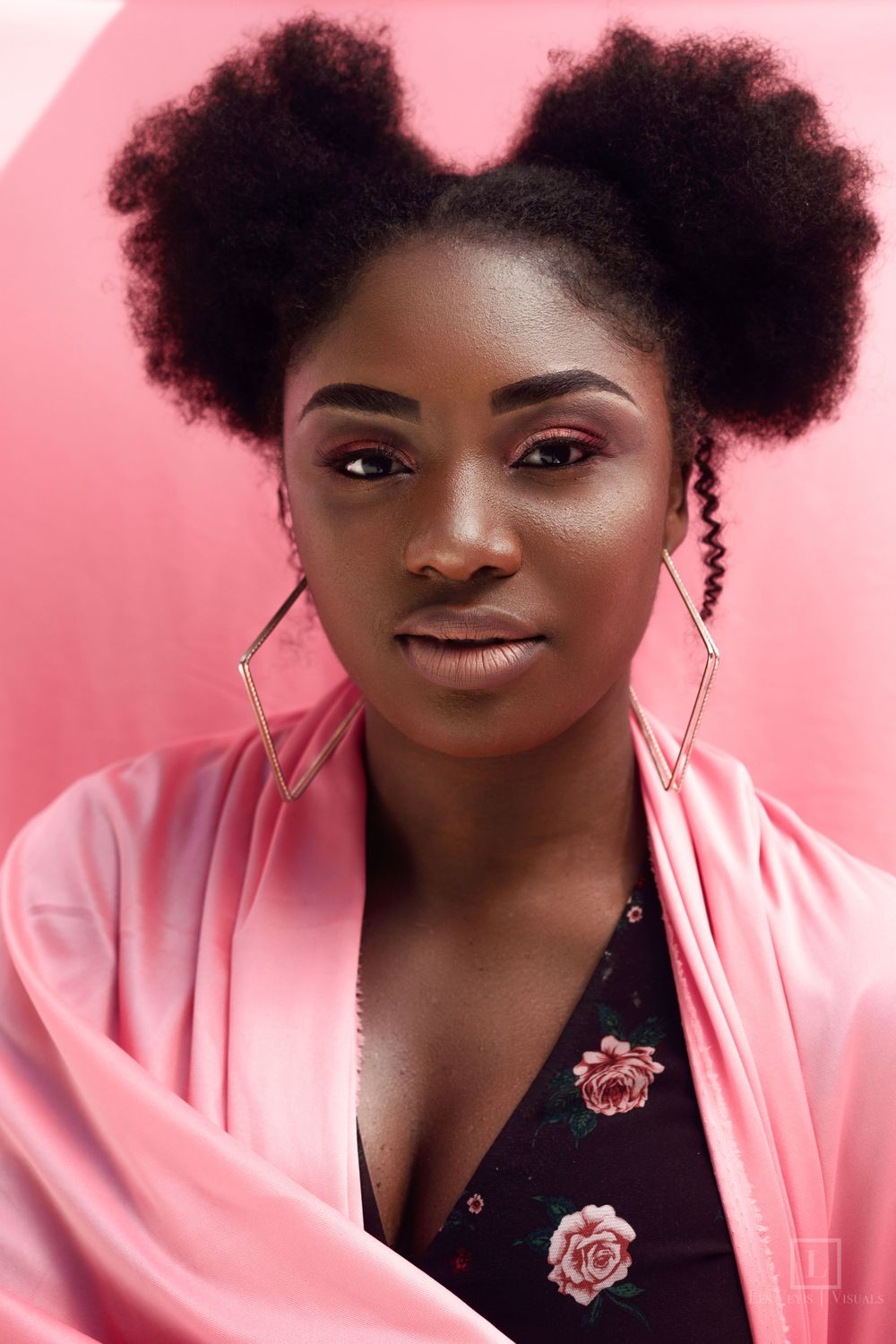 Beauty portrait with afro puffs hairstyle and pink jacket against rosy background.
