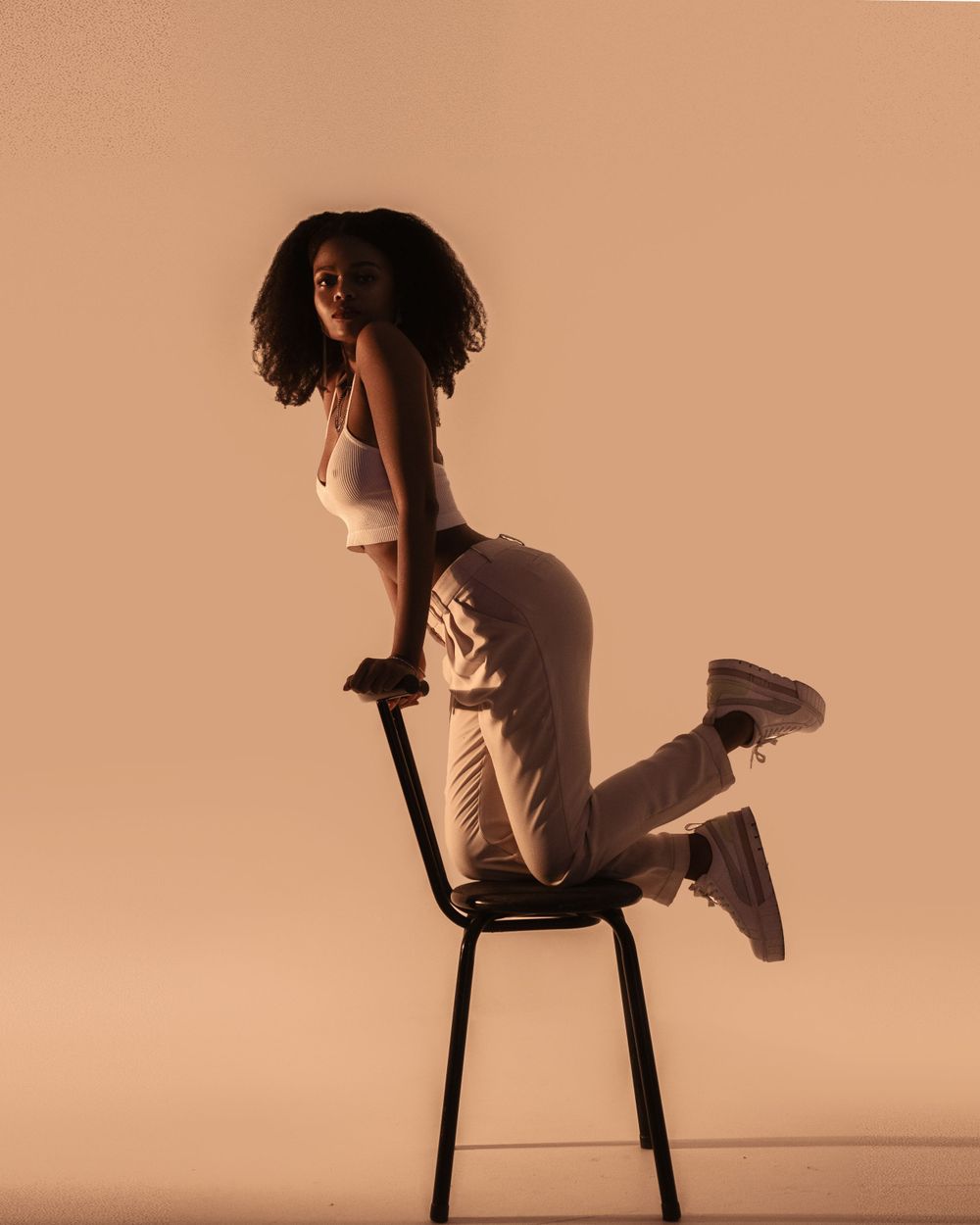 Athletic figure in white outfit striking dynamic pose on chair in warm lighting.