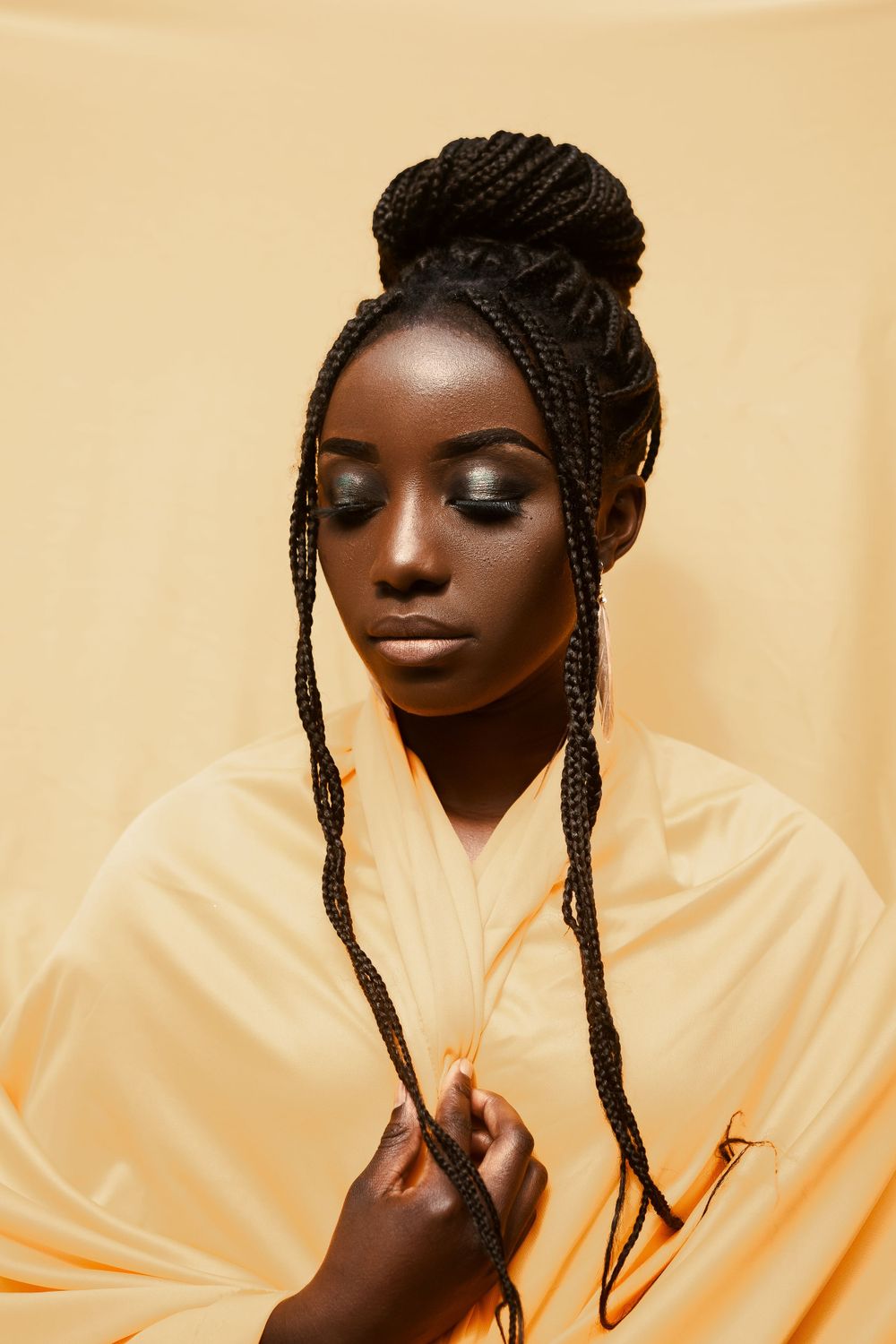 Artistic fashion portrait with braided updo hairstyle against warm yellow background.