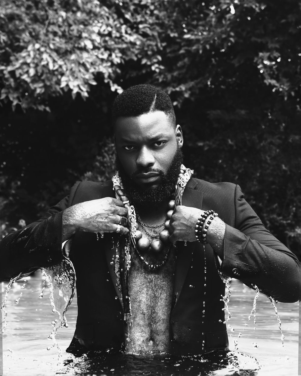 Dramatic black and white portrait of man in suit with jewelry emerging from water.