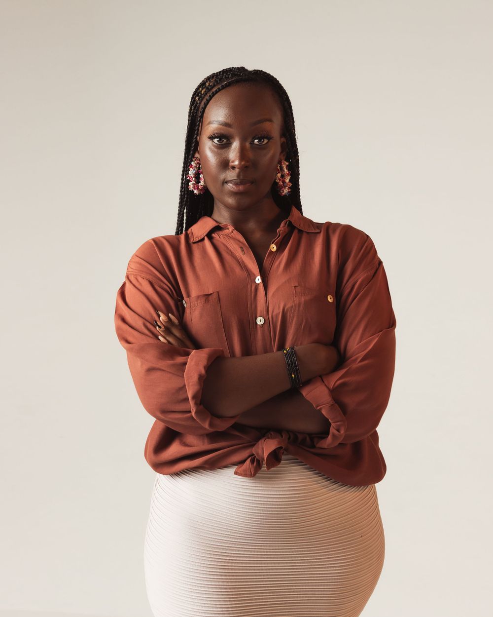 Portrait in rust-colored button-down shirt and textured white skirt against neutral backdrop.