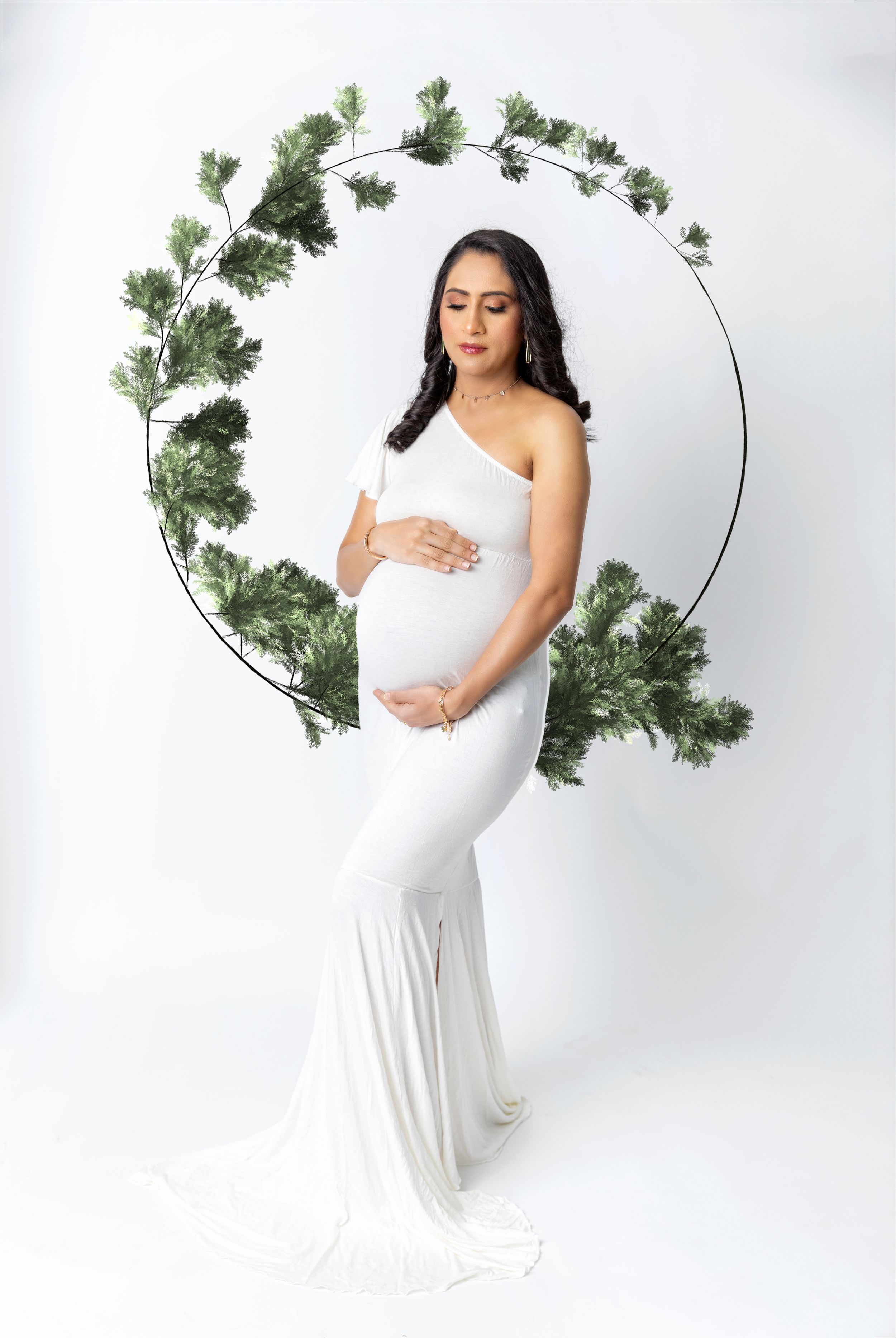 Elegant maternity portrait with white gown and decorative greenery hoop backdrop.