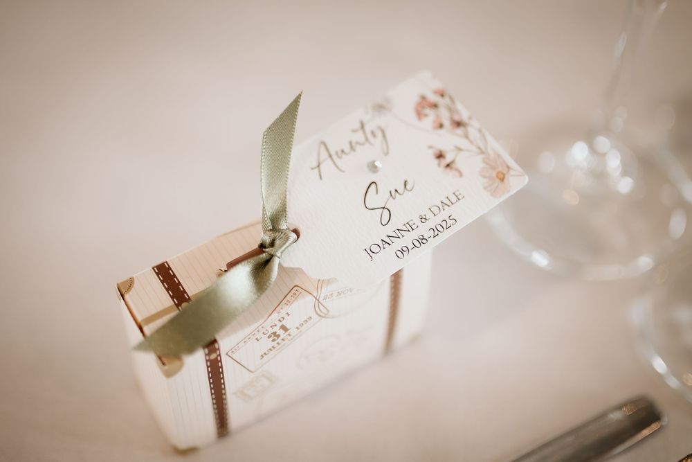 An elegant wedding place card with a green ribbon tied around it sits on a soft beige background.