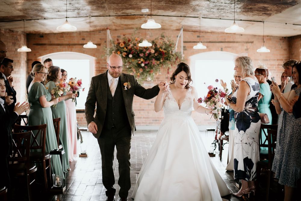 Newlyweds share their first dance in a rustic barn venue surrounded by wedding guests and twinkling lights.