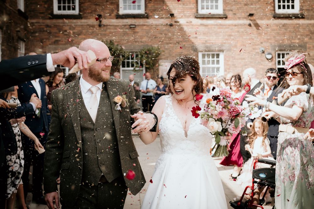 Wedding guests shower newlyweds with confetti outside a historic brick building during a joyful celebration.