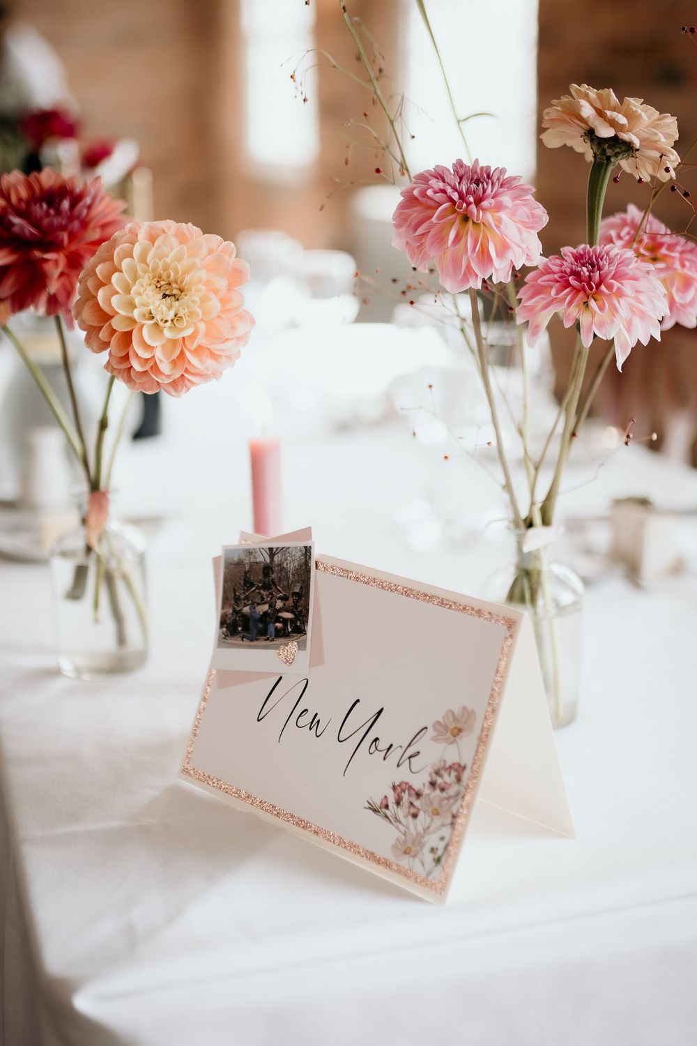 Pink and peach dahlias in glass vases with a New York table card on white linen.