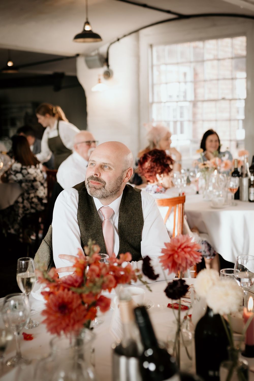 Wedding reception table settings with coral dahlias and elegant glassware in a bright industrial venue.