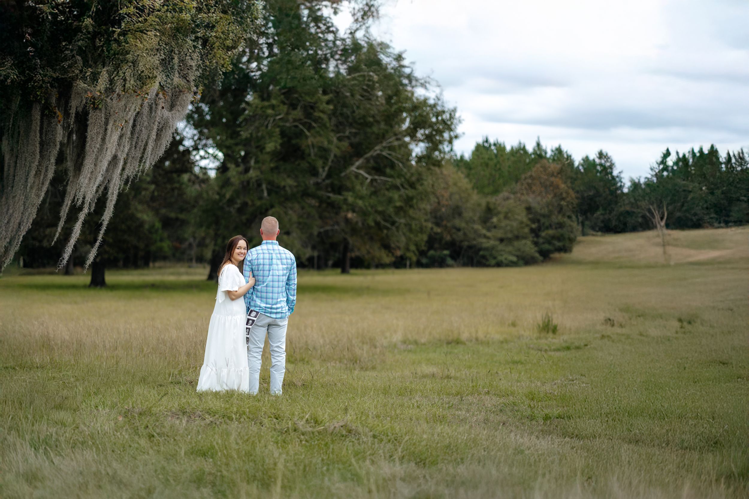A romantic outdoor photo session in a serene meadow with Spanish moss draped trees creating a dreamy backdrop.