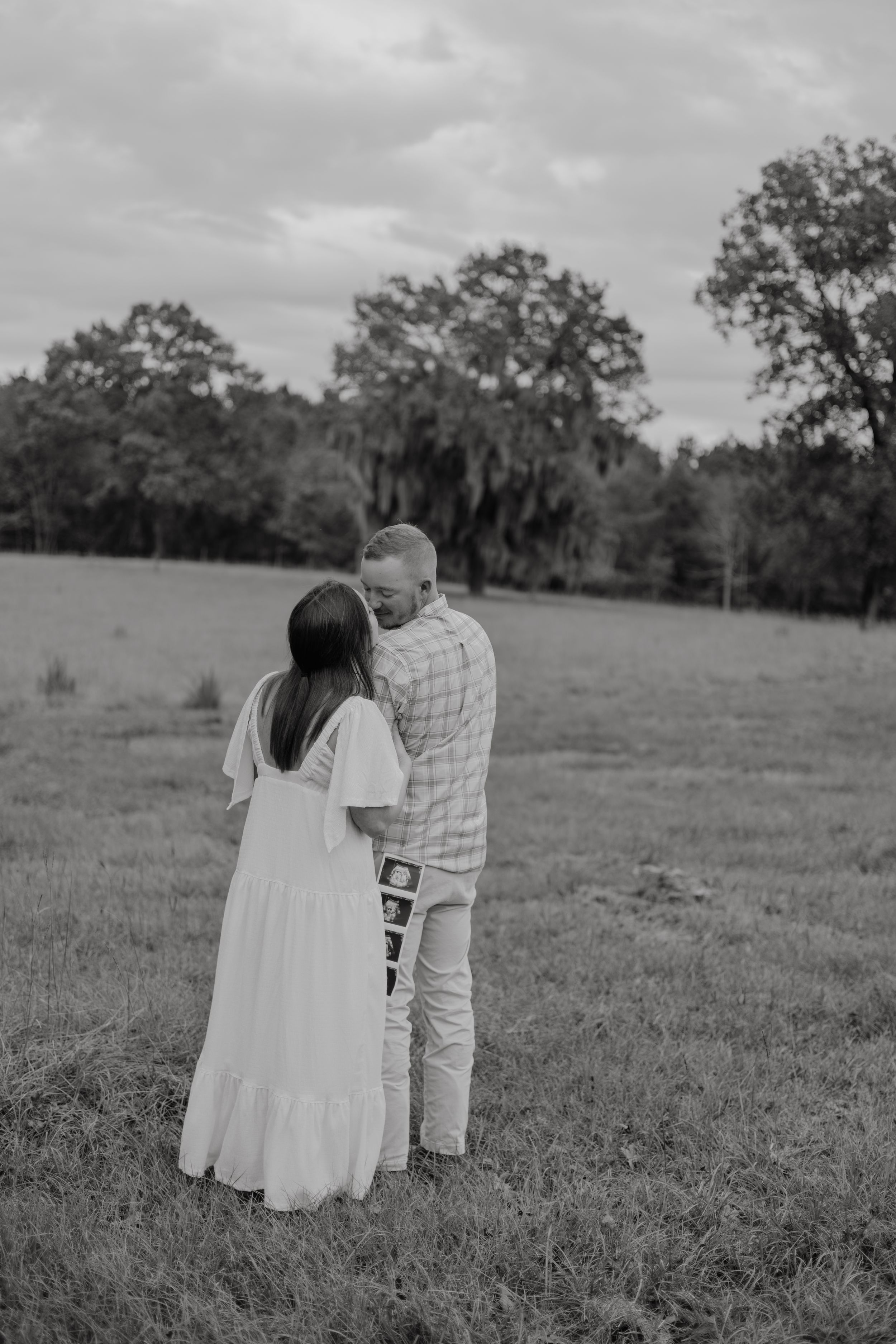 A couple shares an intimate black and white moment together in a serene meadow setting.