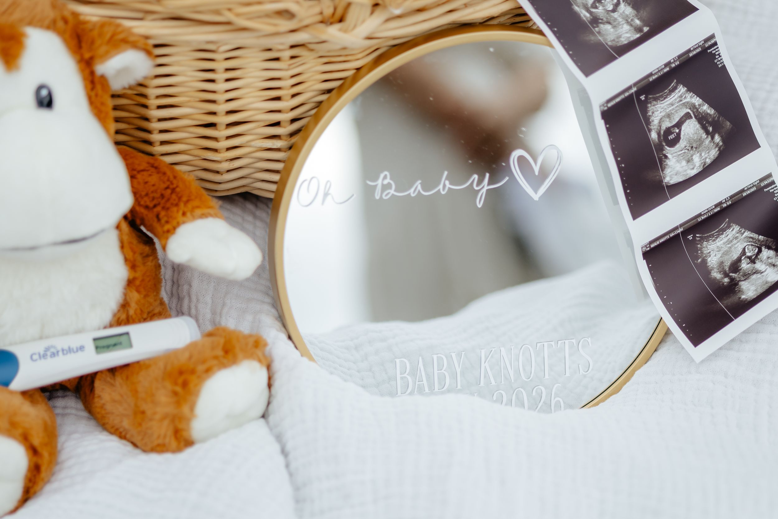 Pregnancy announcement display with ultrasound photos, baby items, and woven basket on white surface with autumn leaves.