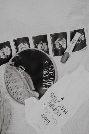 Black and white ultrasound photos arranged with a baby knots disc and handwritten note on white textured surface.