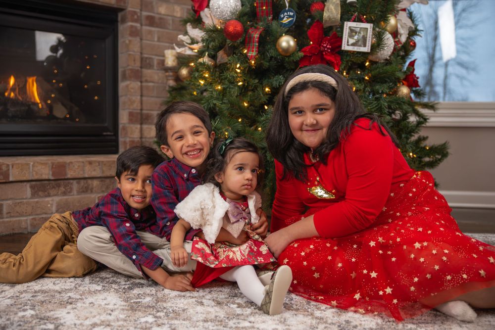 Family group posed by Christmas tree and fireplace in coordinated holiday outfits.
