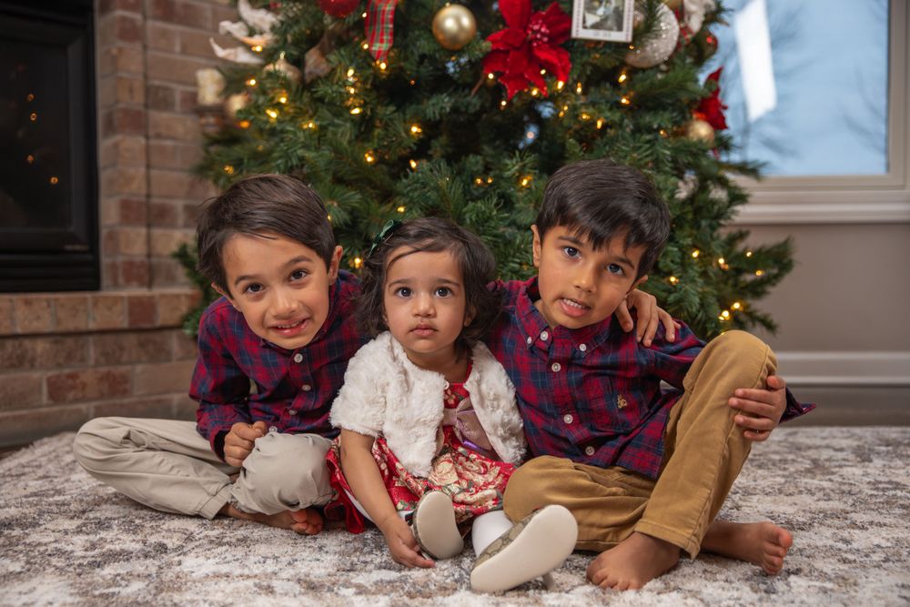 Three siblings in coordinated outfits posing in front of Christmas tree.
