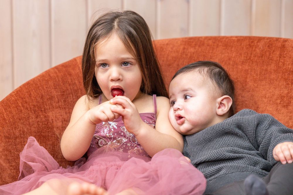 Two young children sitting on orange couch sharing snacks and wearing festive outfits.