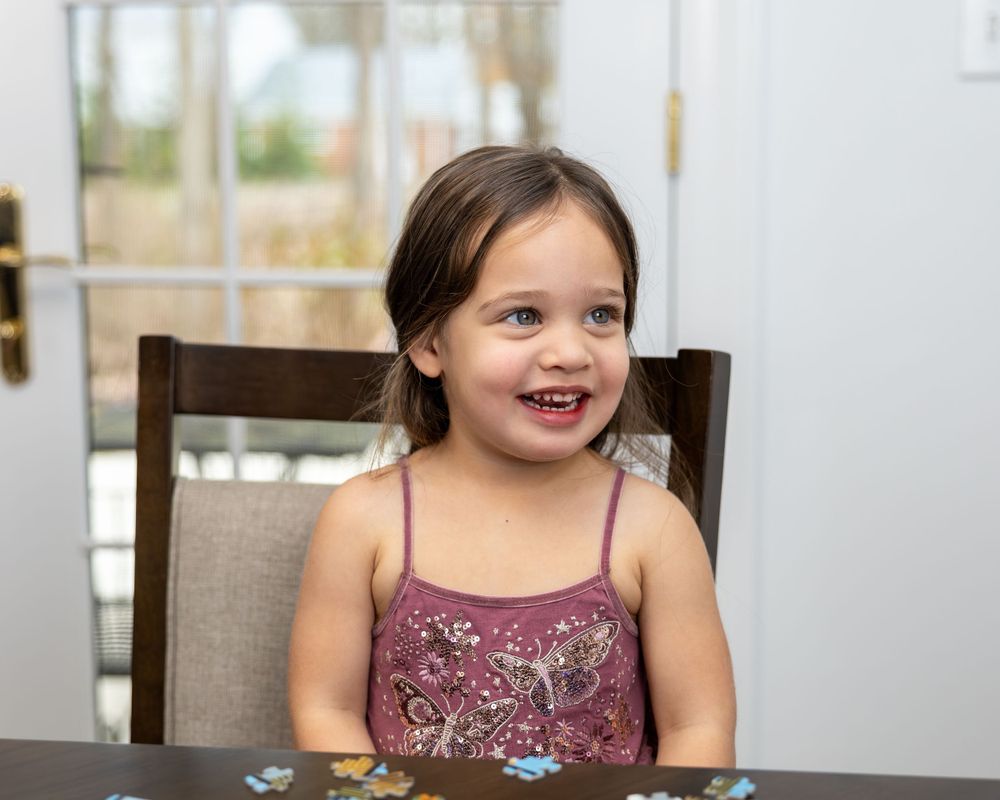 Child in sparkly purple dress sitting at table with bright happy expression.