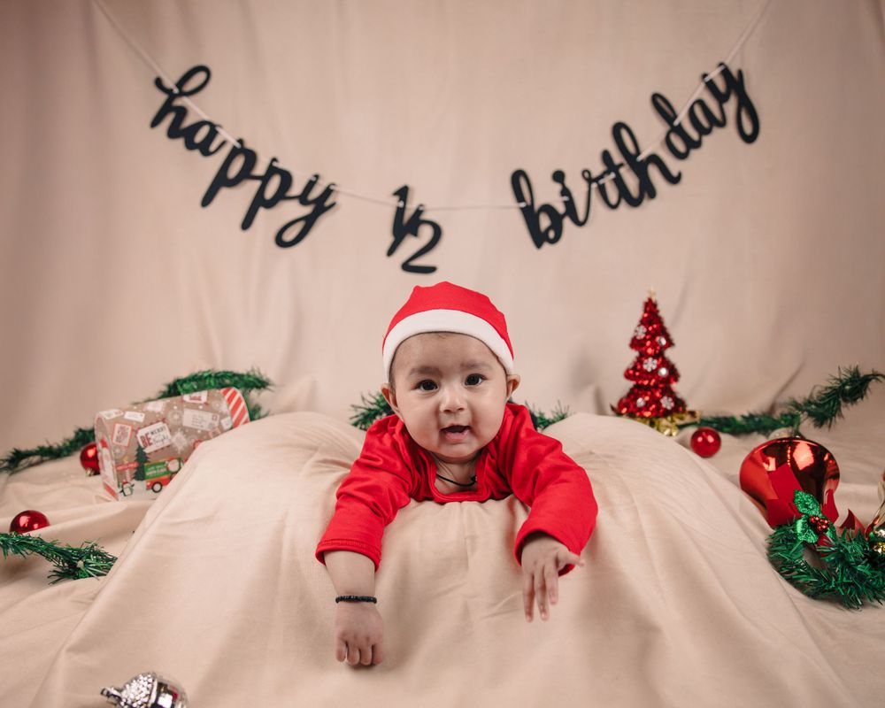 Baby in red holiday outfit and Santa hat at 6 month birthday celebration with Christmas decorations.