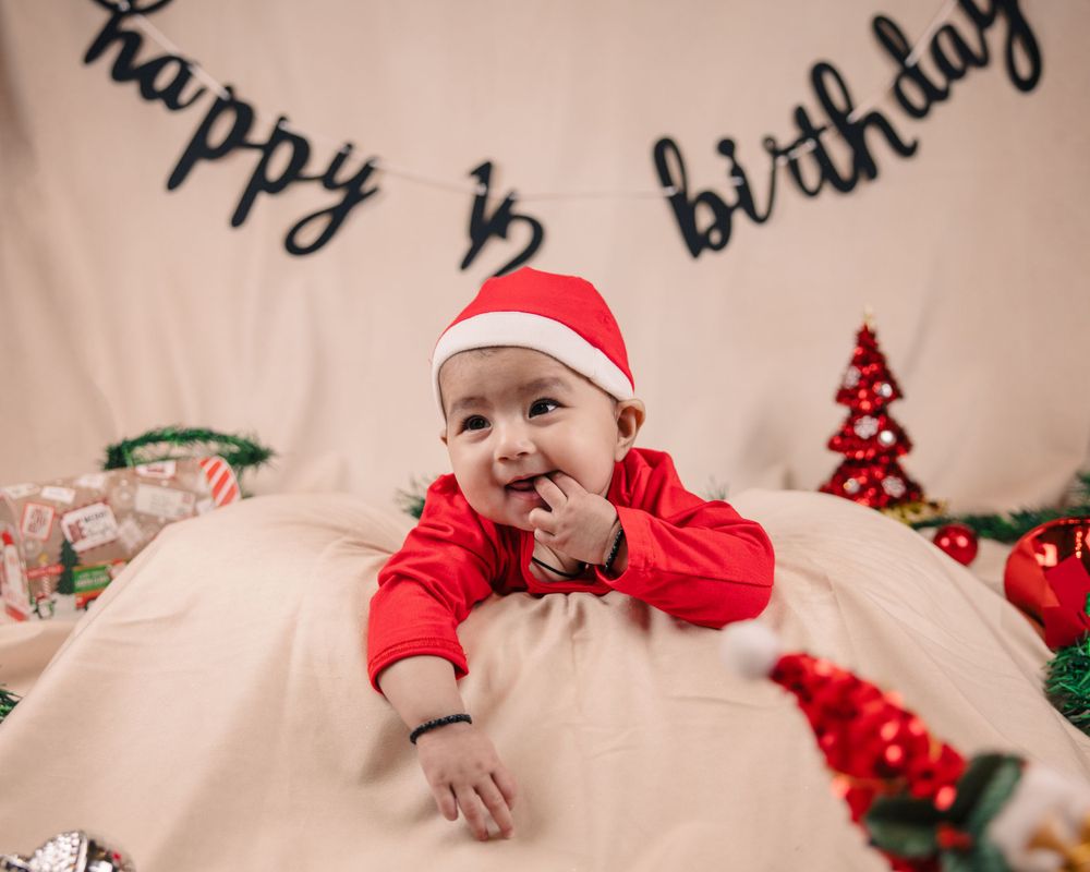 Smiling baby in red holiday outfit under half birthday banner with Christmas decor.
