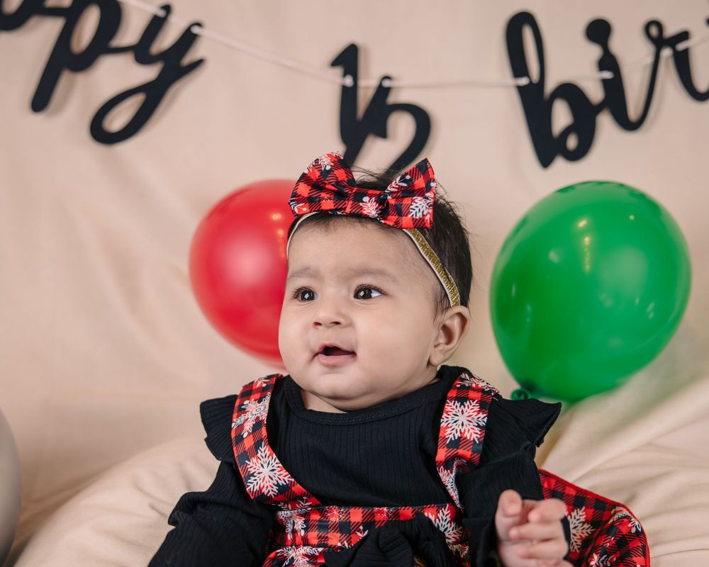 Baby in festive black and red outfit with bow headband at holiday celebration.